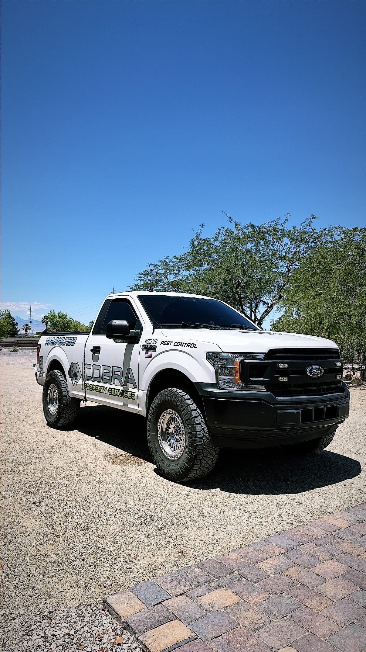 White Ford truck with Cobra Property Services decals parked on gravel under a clear sky.